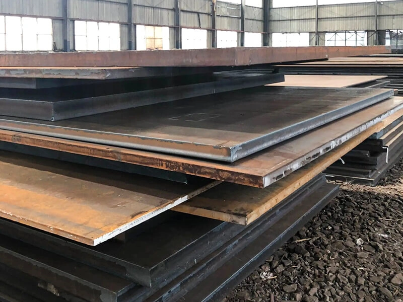 Large stacks of steel plates in a warehouse with a worker standing nearby for scale